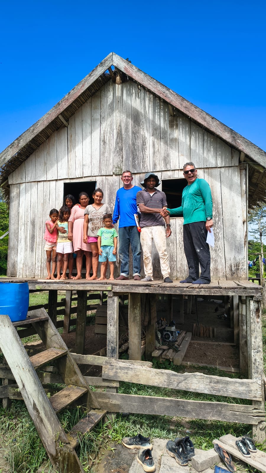 Famílias em frente à casa de madeira, durante visita da equipe